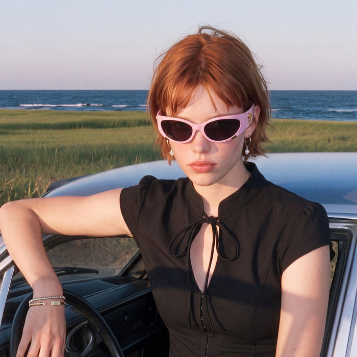 Model wearing pink Cail sunglasses beside a car by the coast